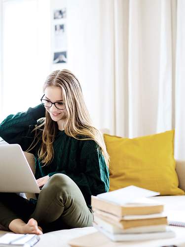 Eine junge Frau sitzt auf der Couch und vergleicht mehrere Zahnzusatzversicherungen im Internet.