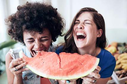 Zwei Frauen essen lachend Wassermelone.