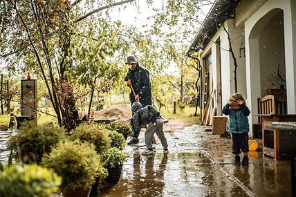 Ein Vater mit Kindern bei Starkregen im Garten.