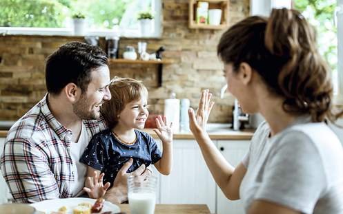 Eine Mutter klatscht mit ihrem Kind und dessen Vater am Küchentisch ab.