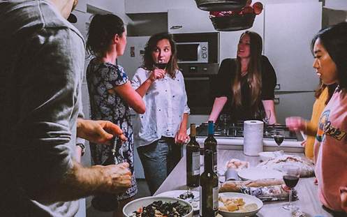 Eine Gruppe von Freunden stehen zusammen an einem Tisch, trinken Wein und essen